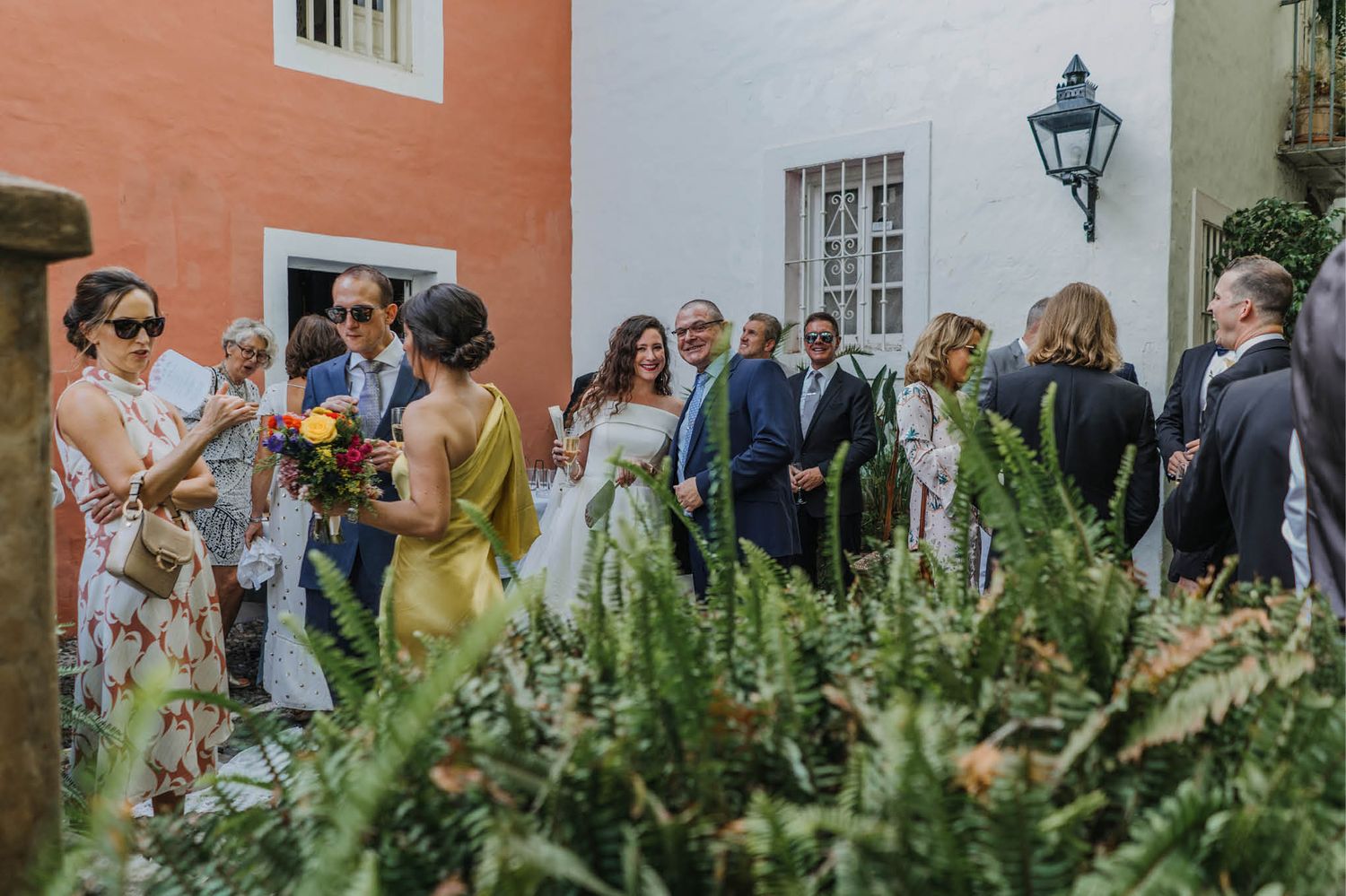Wedding guests mingle in a lush garden courtyard with traditional architecture.