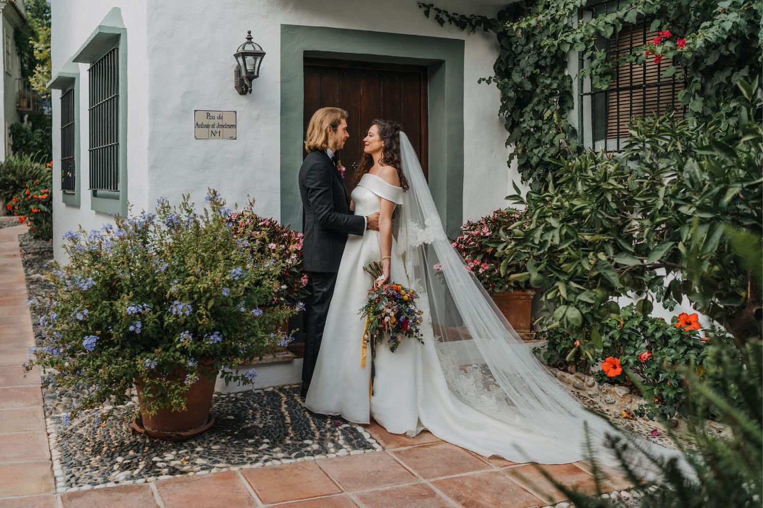 A couple poses in front of a vine-covered doorway with a flowing white veil.