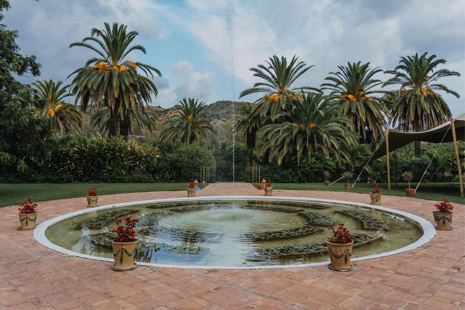 Circular fountain surrounded by palm trees and terracotta tiles in a Mediterranean garden setting.