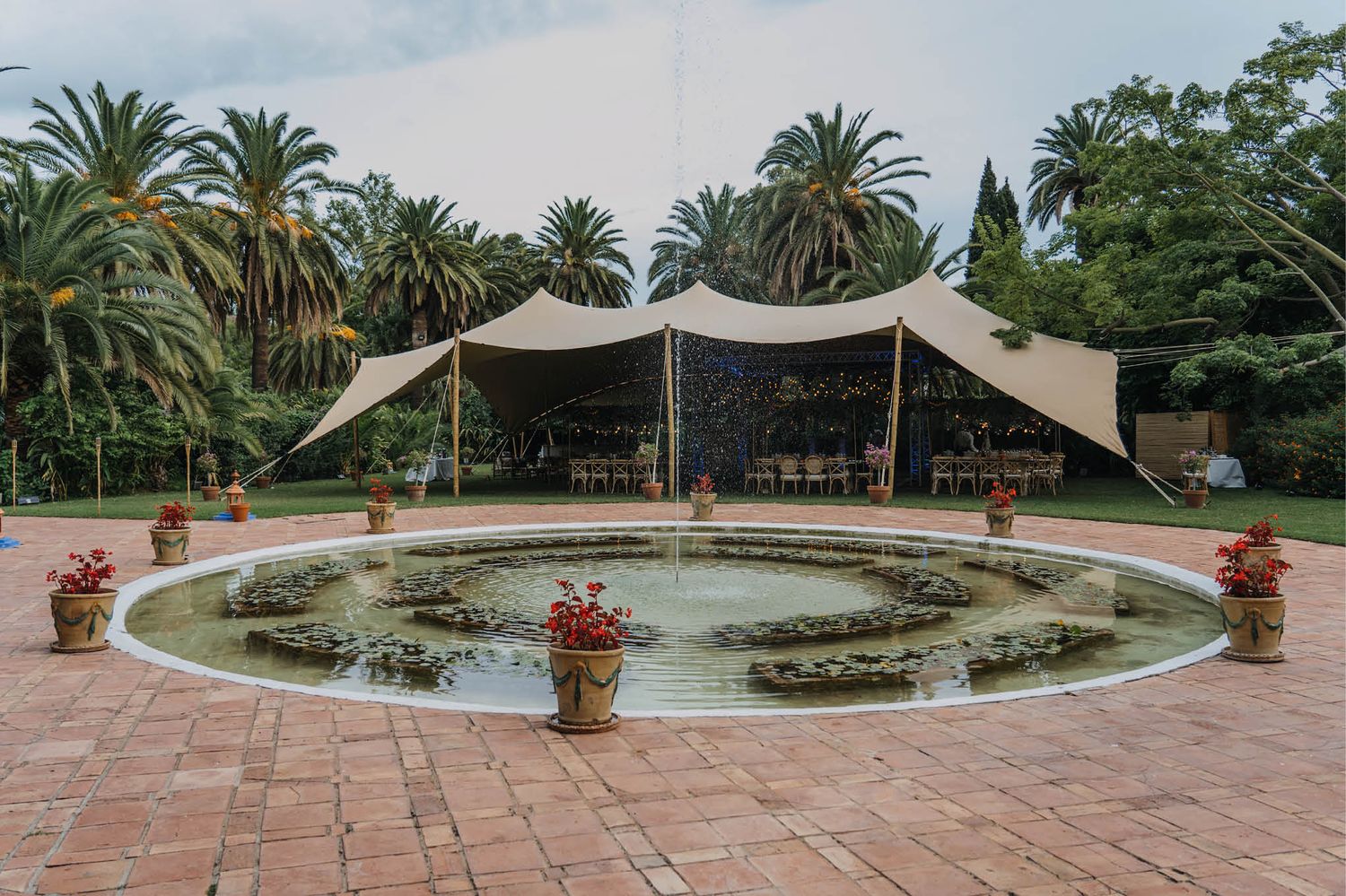 A large circular fountain surrounded by palm trees with a modern stretch tent canopy setup for an outdoor event.