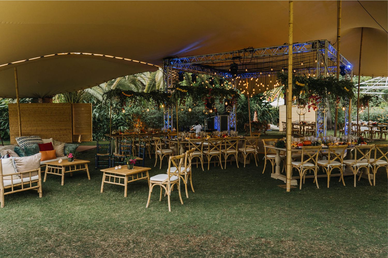 Rustic outdoor wedding reception setup with wooden chairs under a tent canopy with string lights.