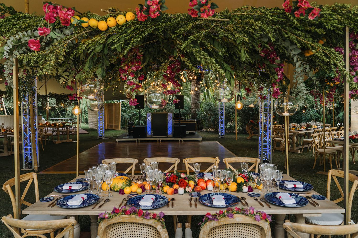 Luxurious table setting under a greenery arch decorated with citrus fruits and pink flowers.
