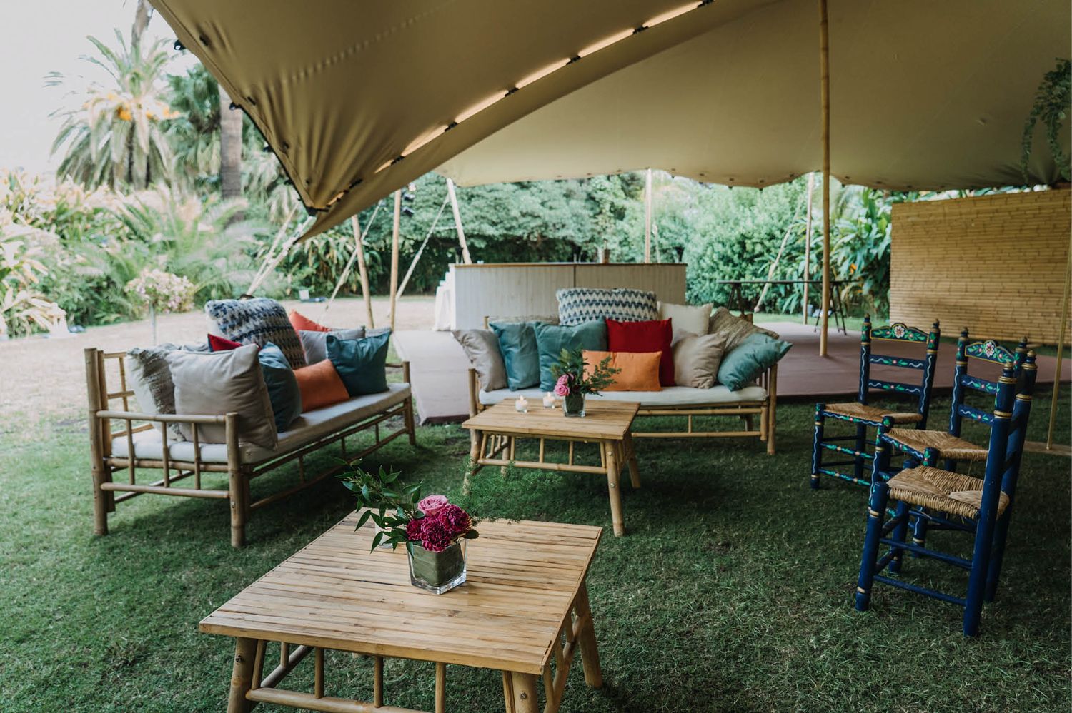 Cozy lounge area setup under a stretch tent with bamboo furniture and colorful throw pillows.