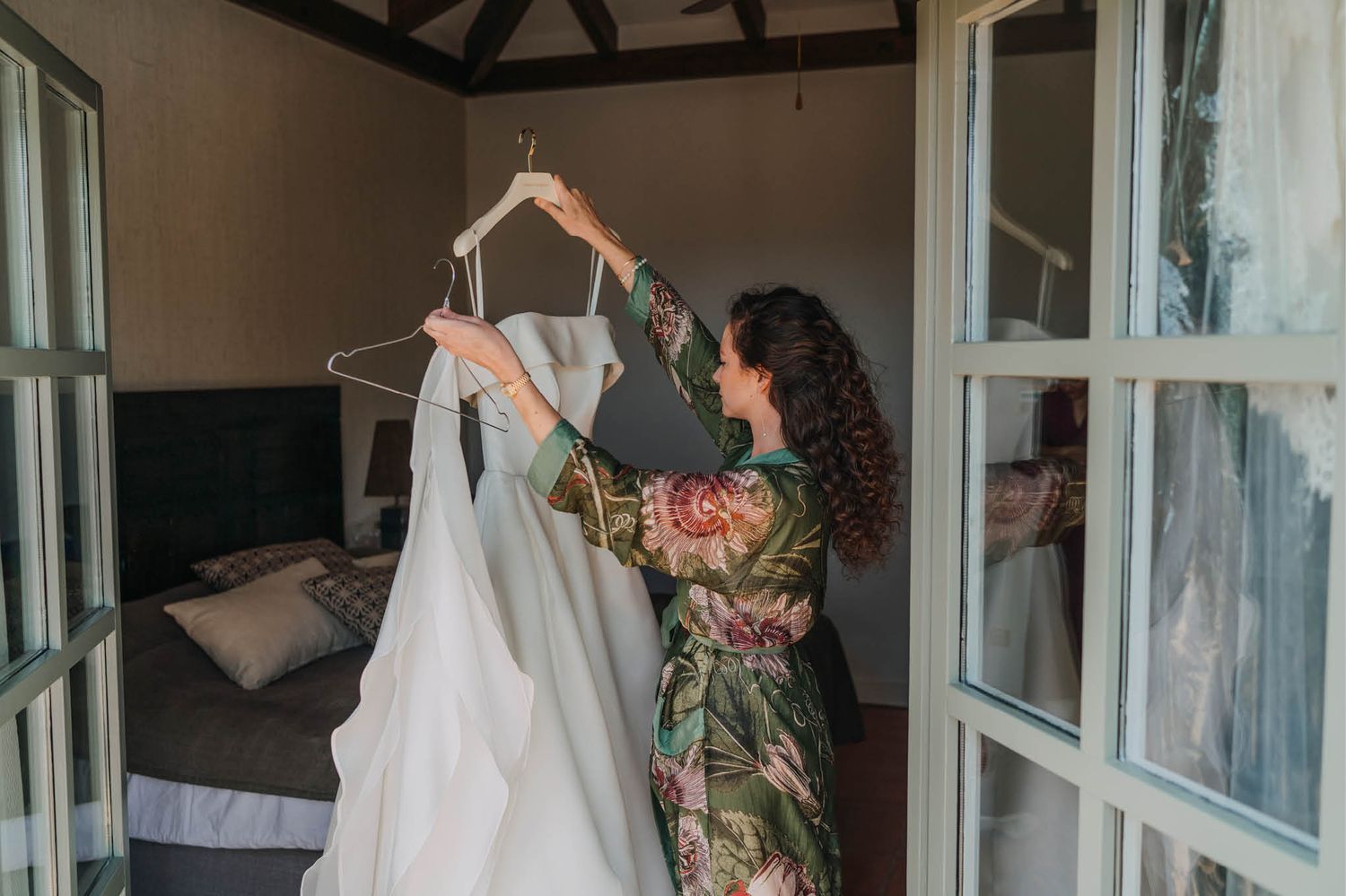Someone in a floral robe handling a white wedding dress on a hanger.
