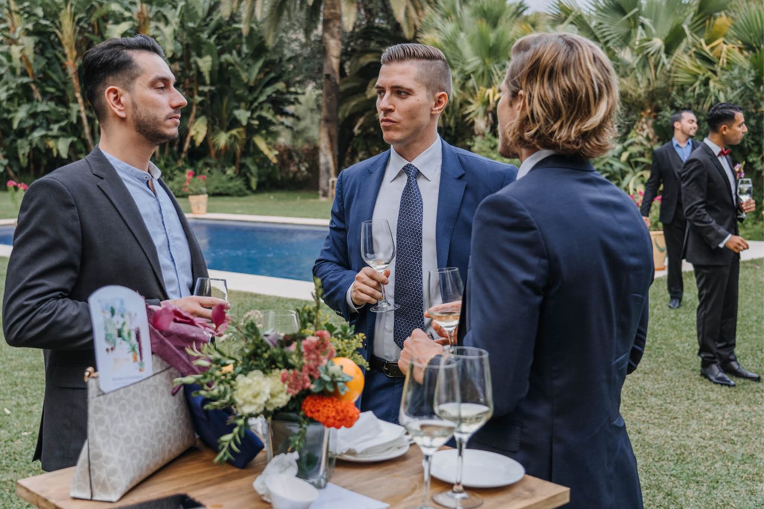 Guests engaged in conversation at an outdoor reception table by the pool.
