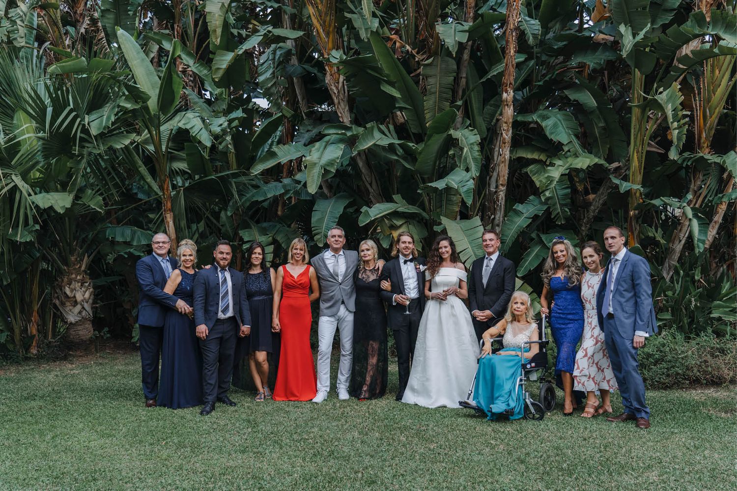 Wedding party posing for a formal group photo in a tropical garden setting.