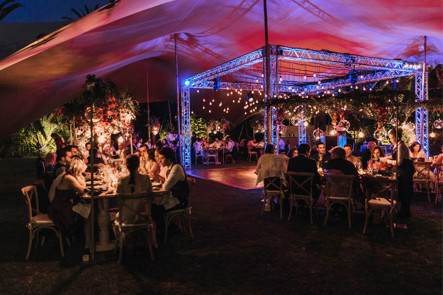Wedding reception under tent with ambient lighting and guests seated at dinner tables.