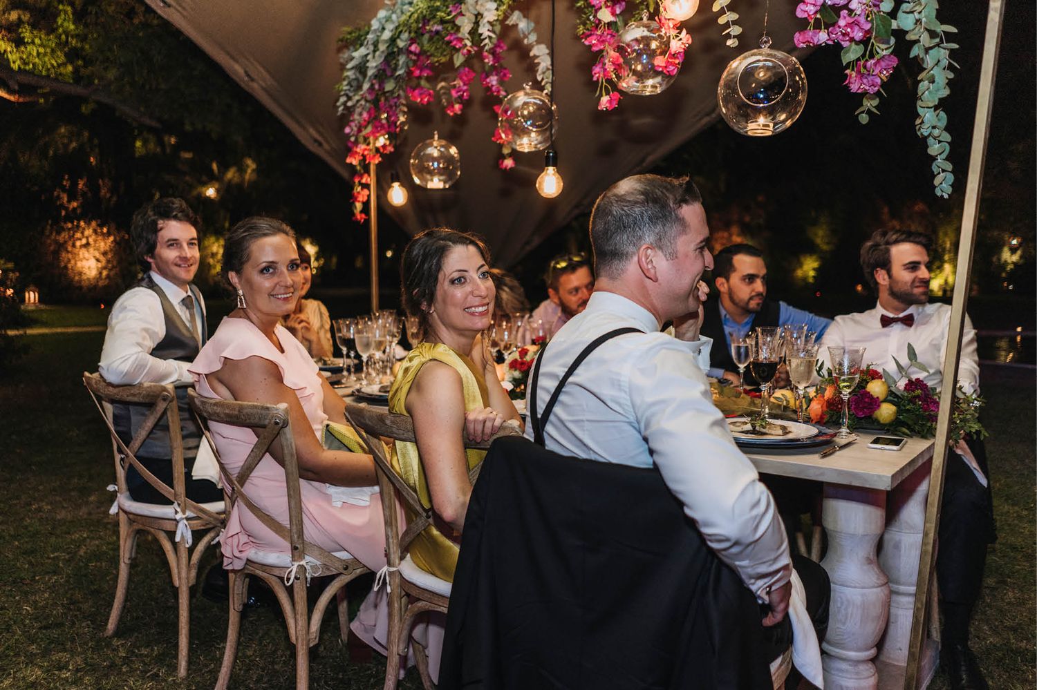 Wedding guests enjoying dinner conversation at decorated table under outdoor tent.