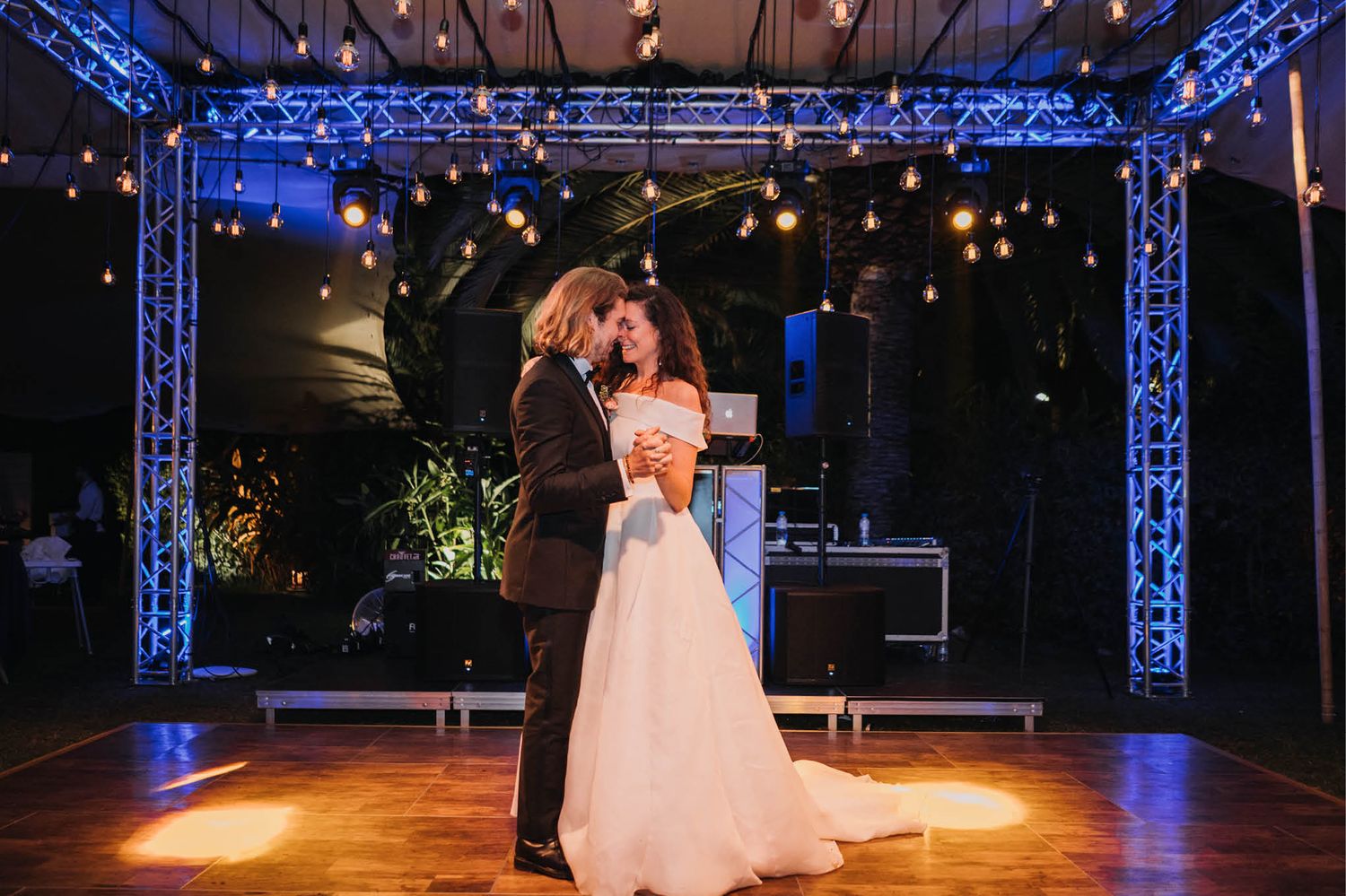 Romantic first dance at a wedding reception under blue lighting and a truss structure.