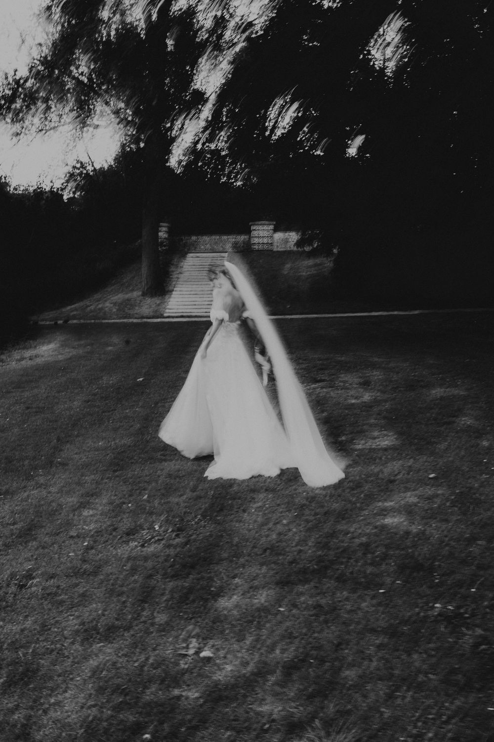A ghostly figure in a white dress moves across a dark grassy field in a series of motion-blurred black and white photographs.
