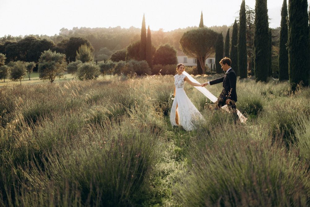 Romantic couple walking through a sunlit Tuscan field of lavender and cypress trees at golden hour.