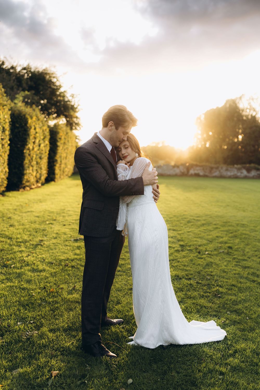 A romantic wedding couple embraces in a sunlit meadow during golden hour at sunset.