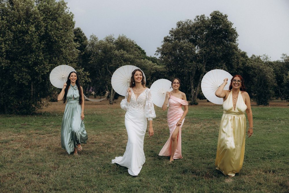 A group in flowing dresses dances and twirls together in a sunlit meadow during a joyful outdoor celebration.