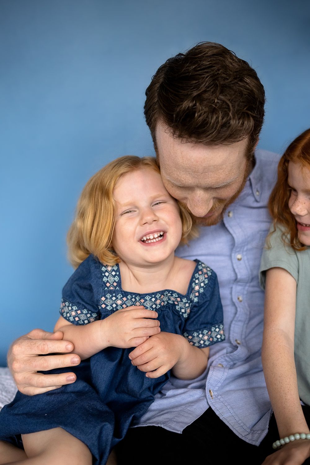 Family sharing playful moments together against blue backdrop.