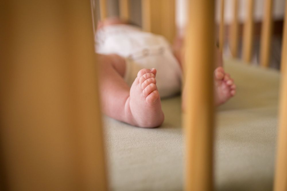 Close-up view of tiny baby feet seen through wooden crib slats in warm lighting.