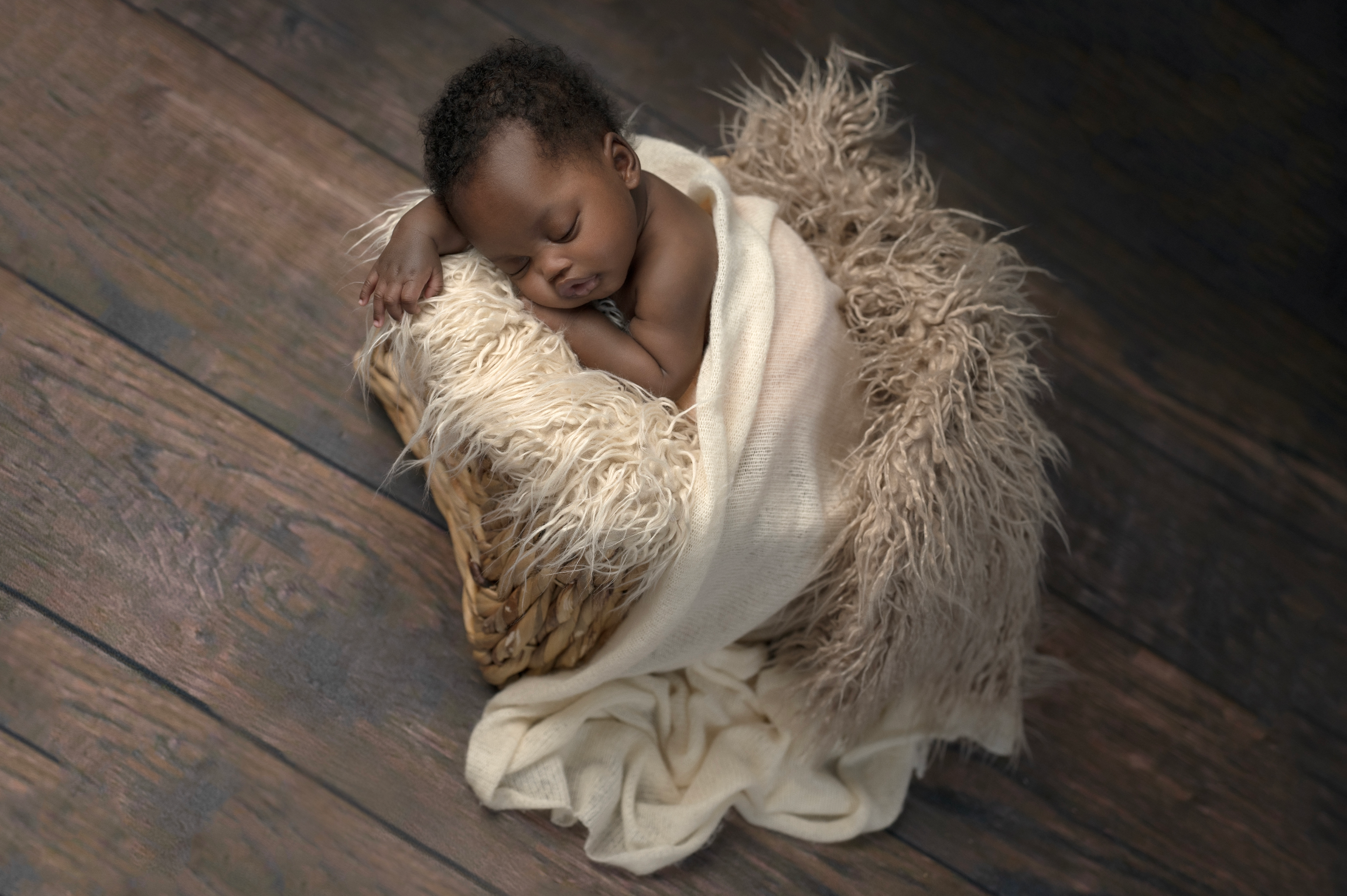 Newborn baby sleeping peacefully wrapped in cream fabric on a rustic wooden floor. Embracing Life’s Beauty