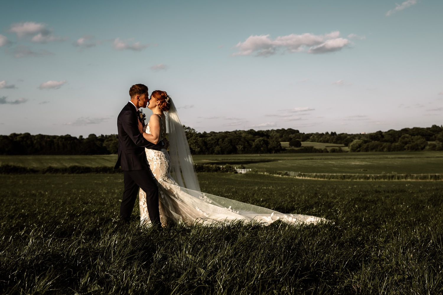 Romantic wedding couple embracing in a scenic field at sunset.