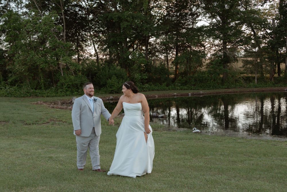 Newlyweds walking hand in hand by a pond during golden hour.