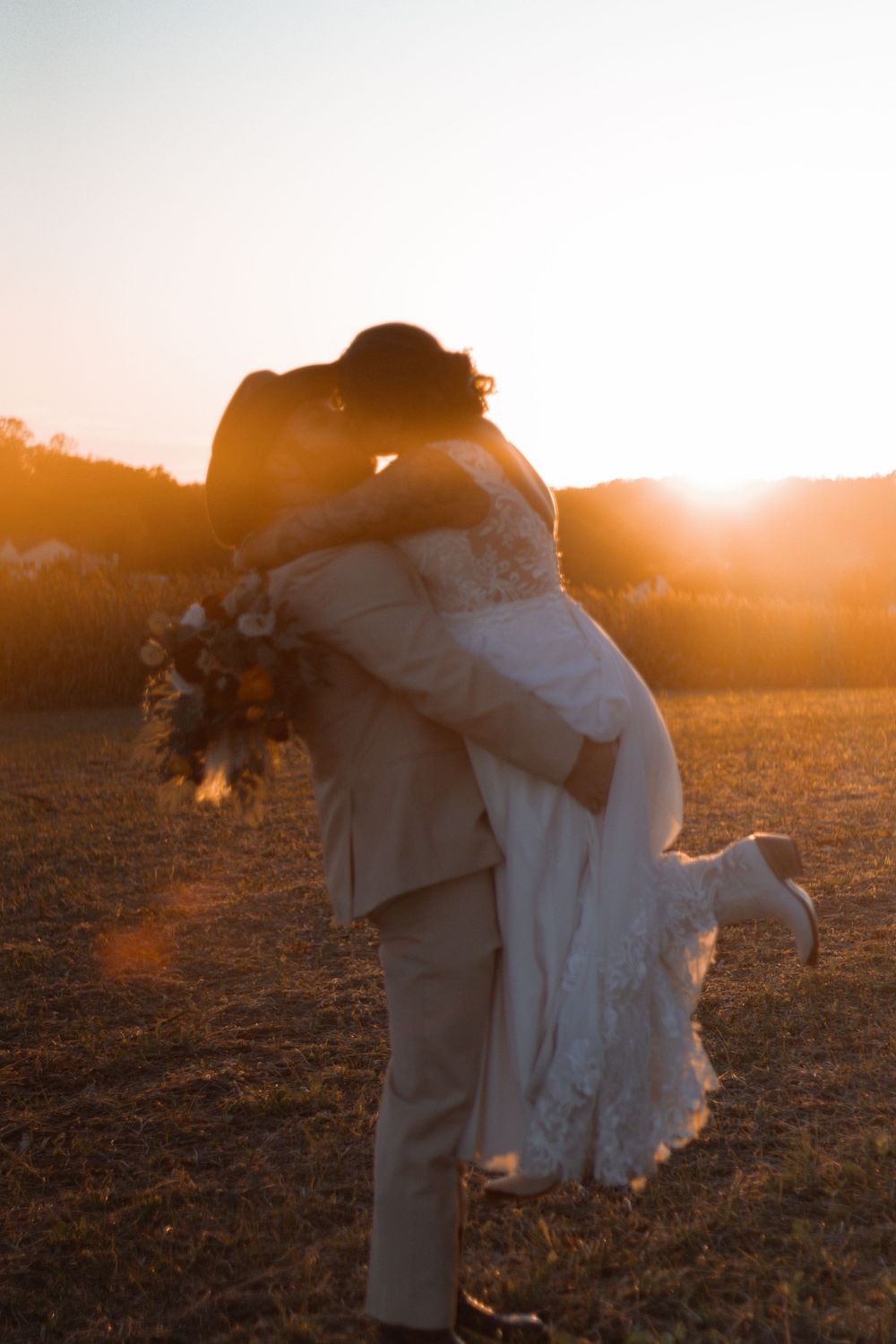 Newlywed couple sharing an intimate moment at golden hour in a rustic field setting.