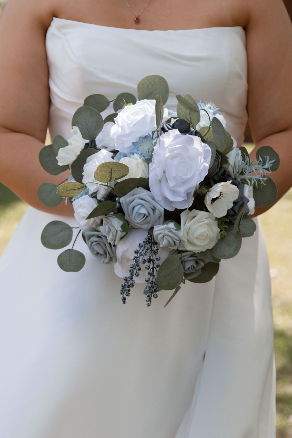 Wedding bouquet with white roses and eucalyptus leaves held against a white dress.