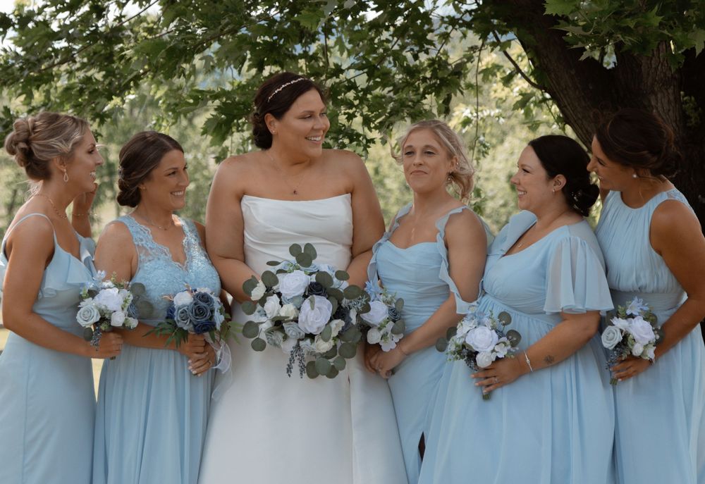 Bridal party in light blue dresses holding matching white and blue bouquets.