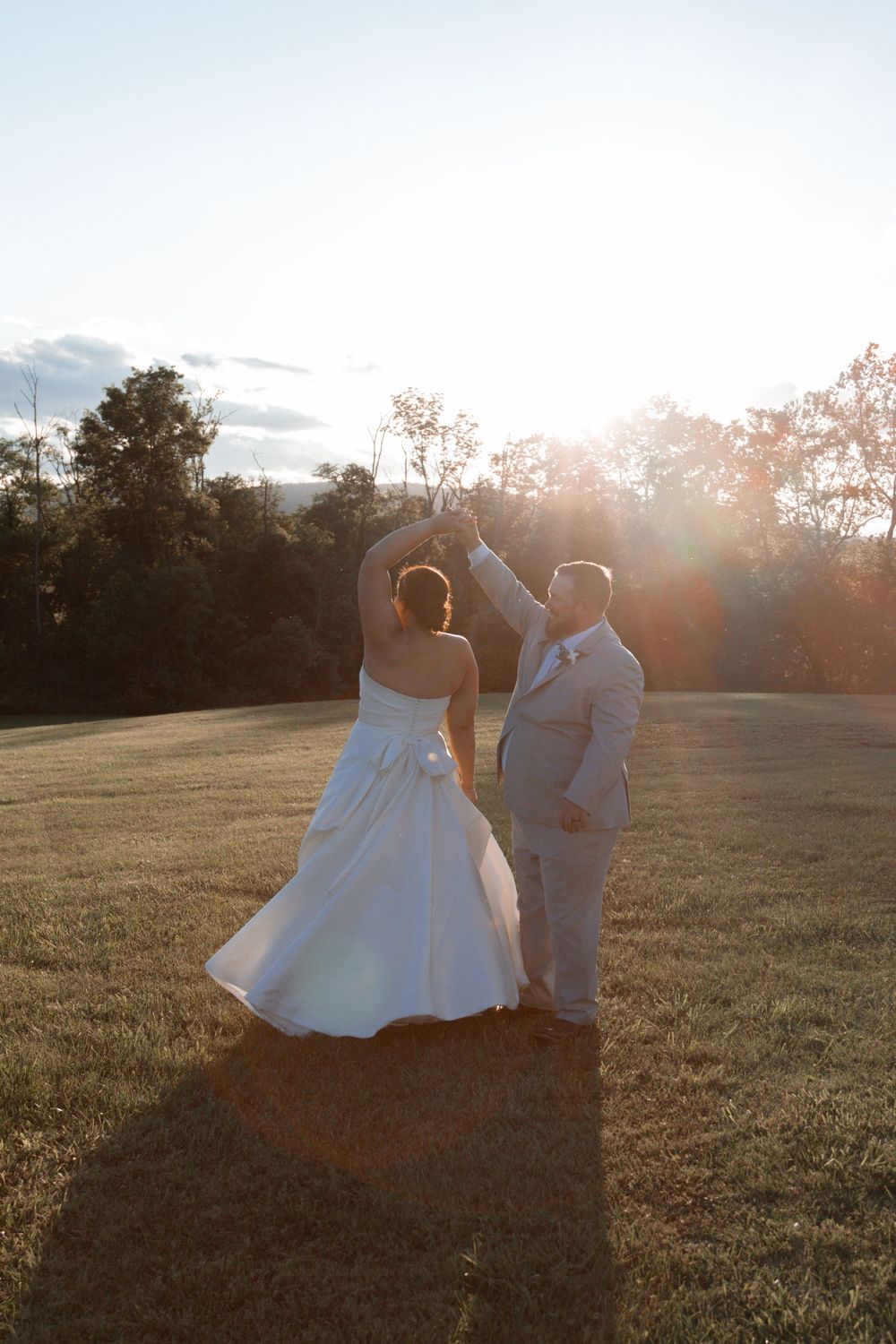 Couple dancing in wedding attire during sunset in an open field.