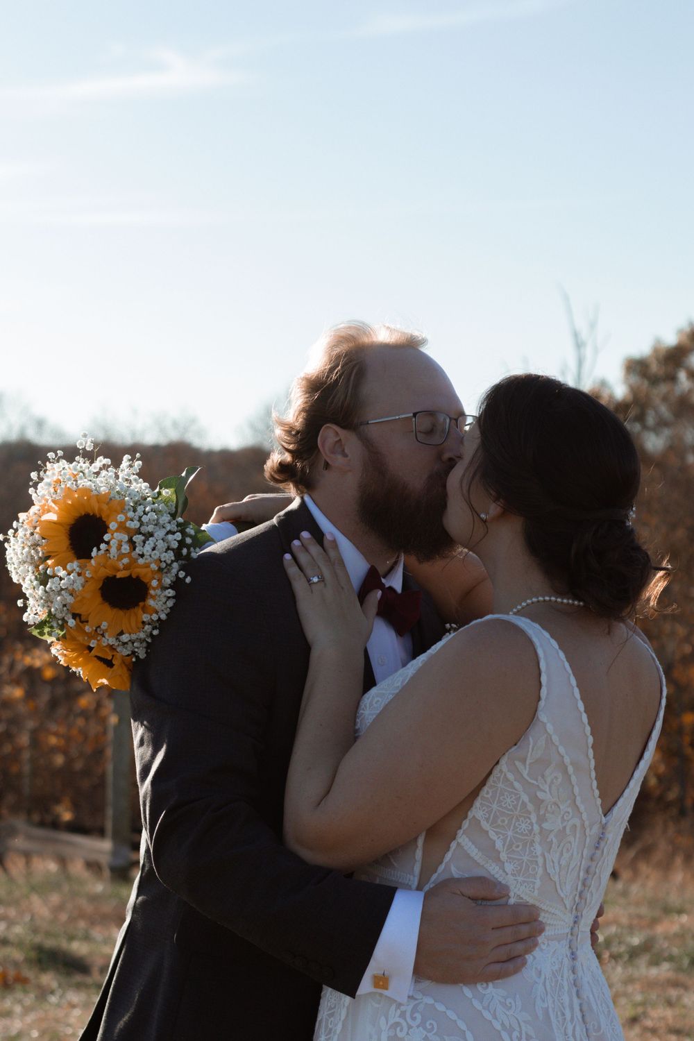 Rustic outdoor wedding celebration with sunflower bouquet against autumn backdrop.