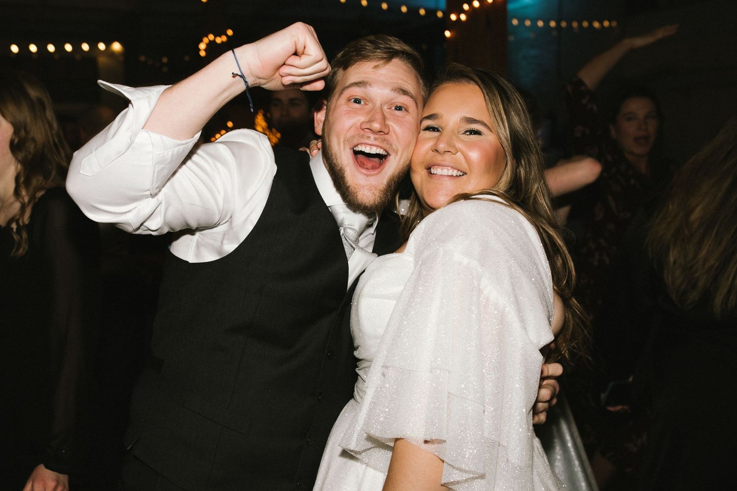 Joyful wedding reception moment captured on dance floor with party lighting.