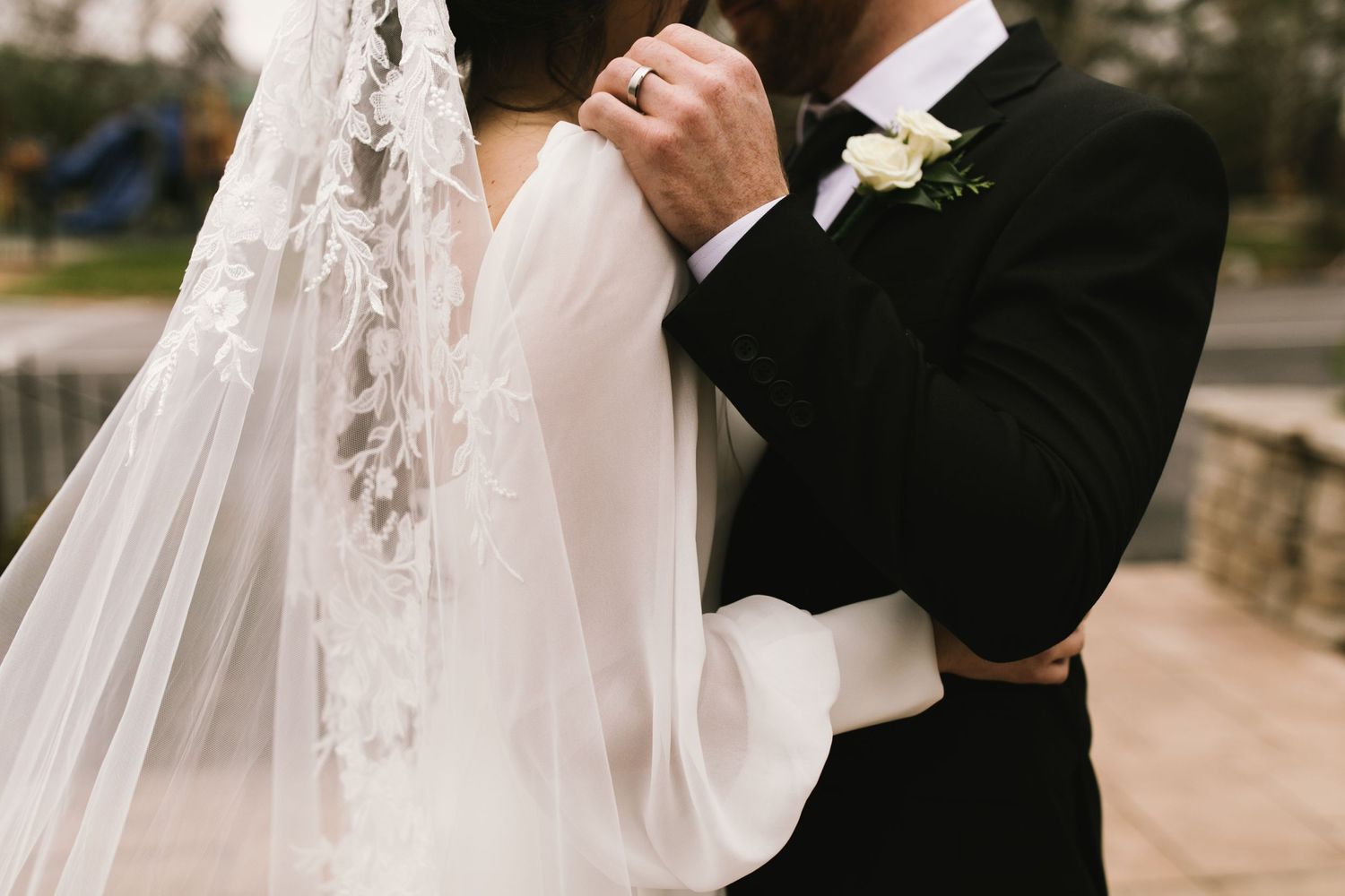 Close-up detail of bride's veil and groom's boutonniere during outdoor wedding moment.