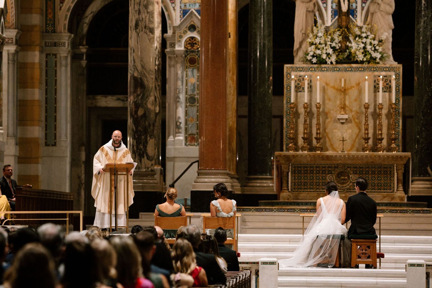 Traditional Catholic wedding ceremony taking place in an ornate cathedral with clergy officiating at the altar.