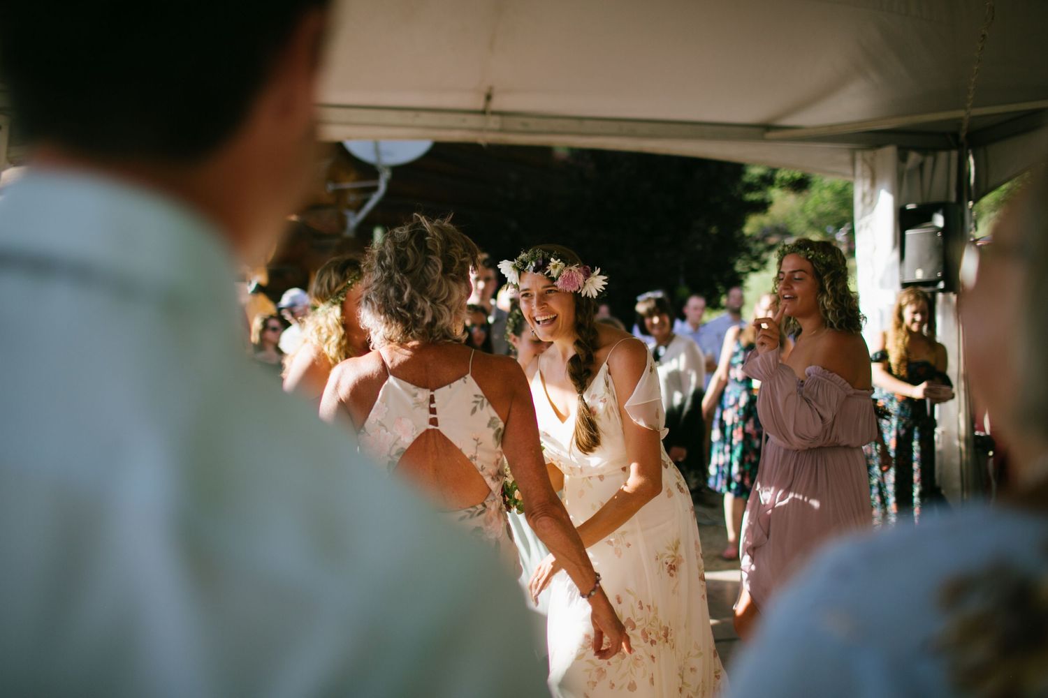 Sun-drenched wedding reception with dancing guests under covered outdoor venue.