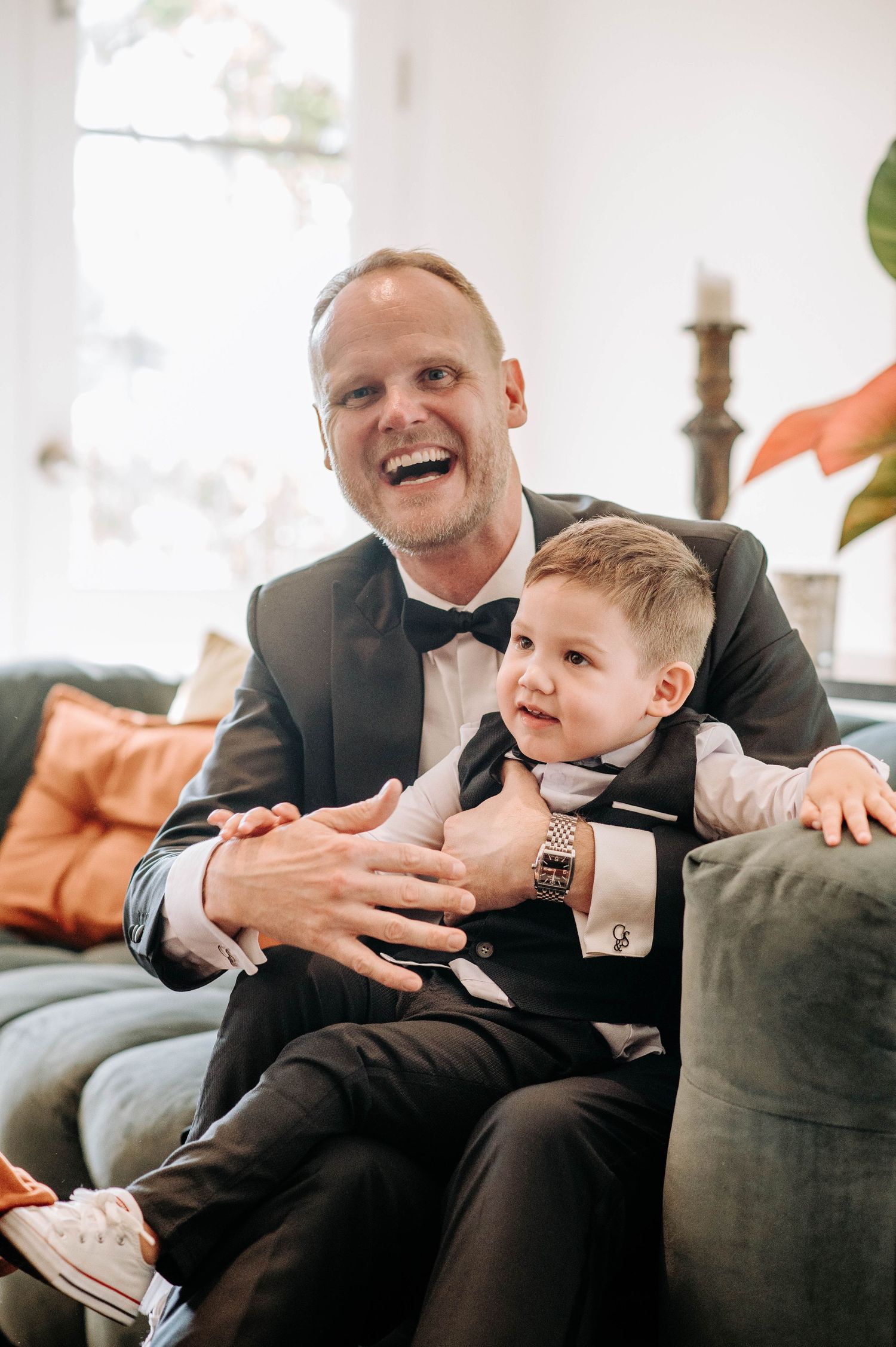 A joyful moment shared on a grey couch with formal attire and warm interior lighting.