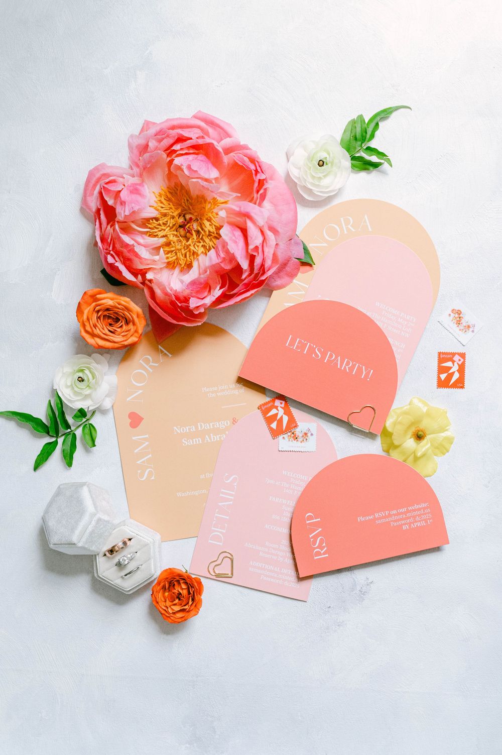 Coral and peach wedding invitation suite with floral accents on white marble background.