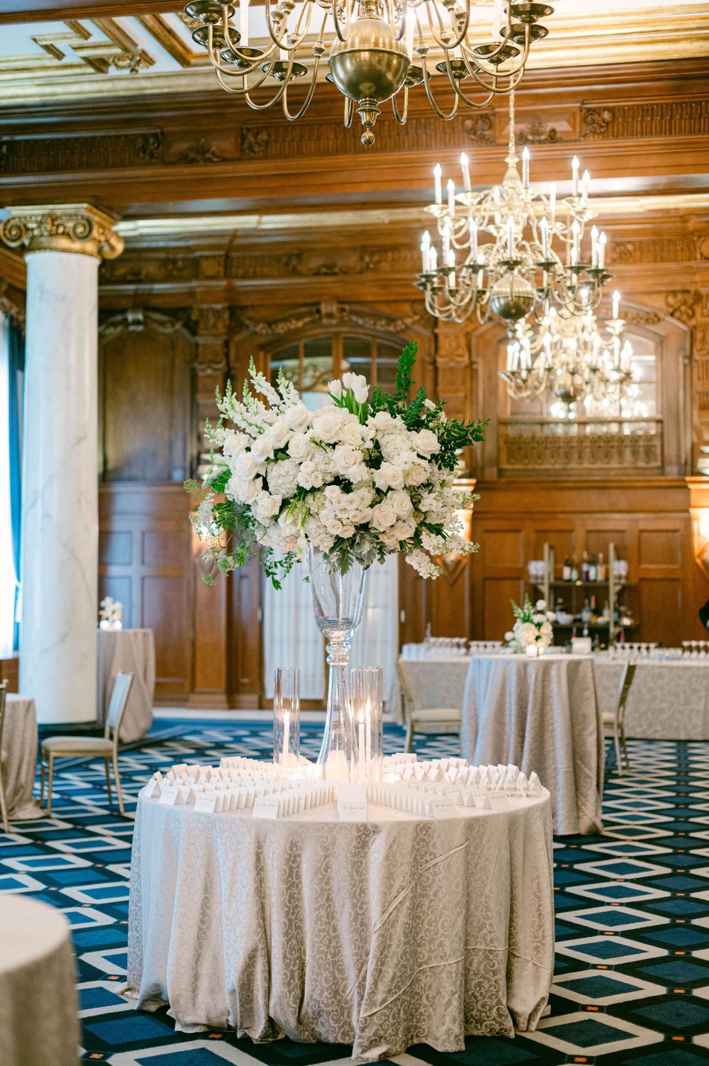 Luxurious ballroom decorated with crystal chandeliers and round tables with white linens.