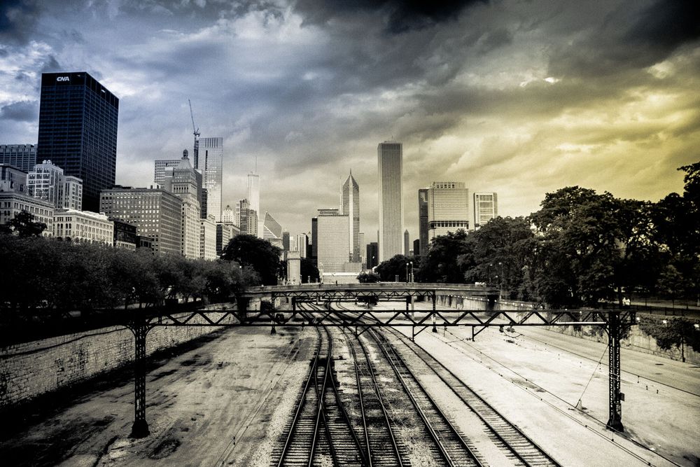 Urban railway tracks leading to Chicago skyline under stormy yellow sunset sky.