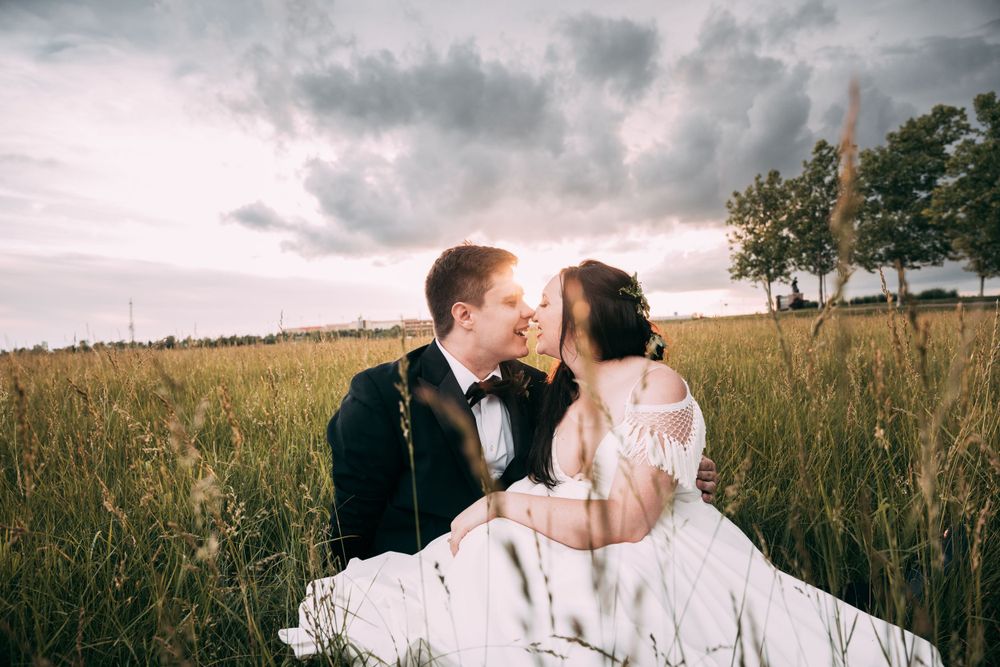 A couple sits in a golden field at sunset wearing formal wedding attire.