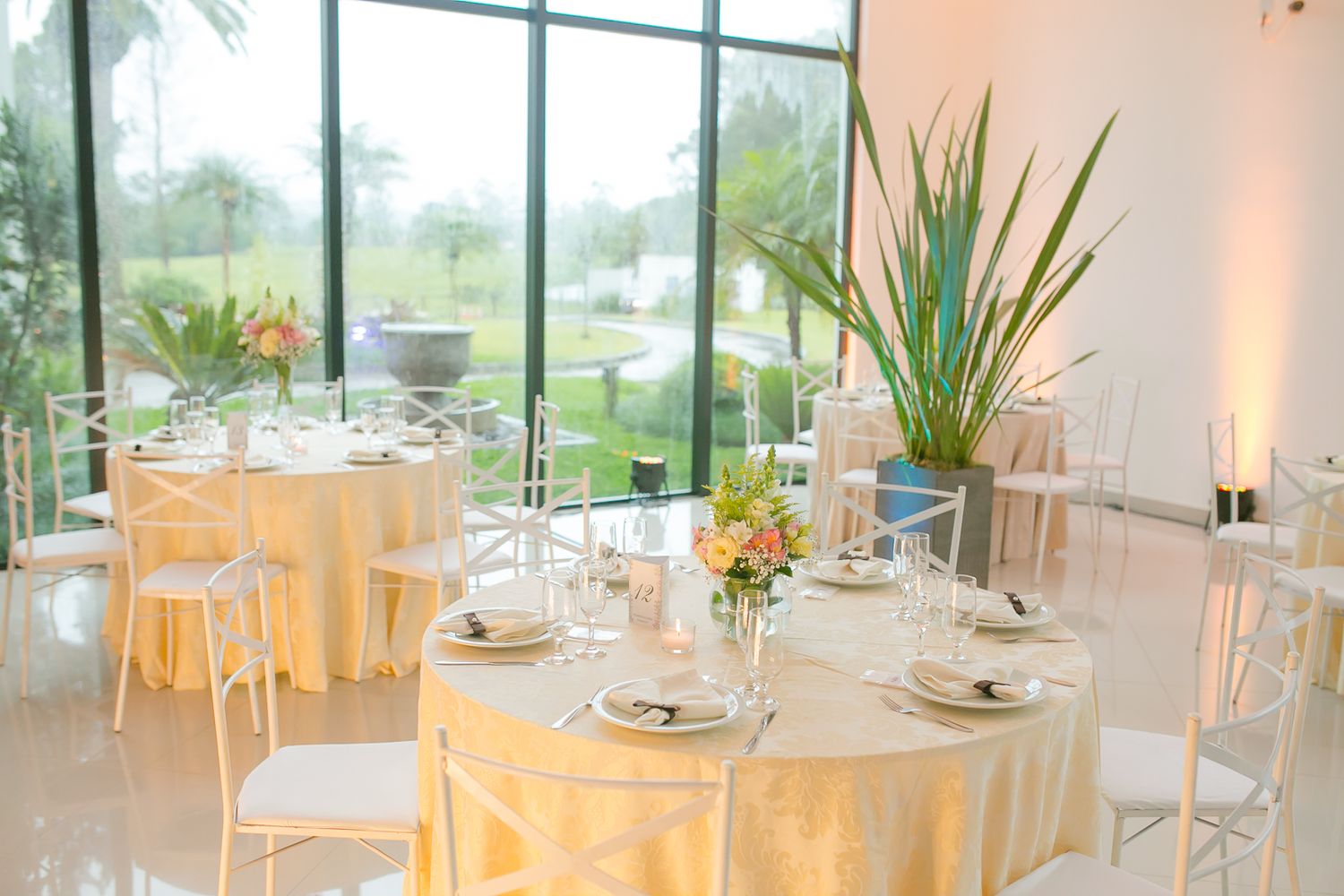 An elegant wedding reception setup with yellow tablecloths and clear chairs in a bright venue.