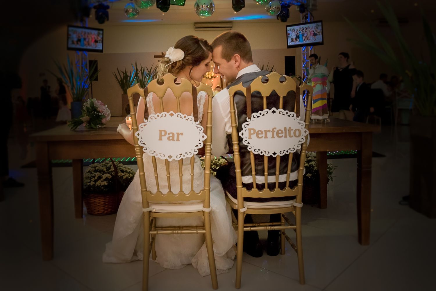 Decorated wedding chairs with 'Par' and 'Perfeito' signs at a reception venue.