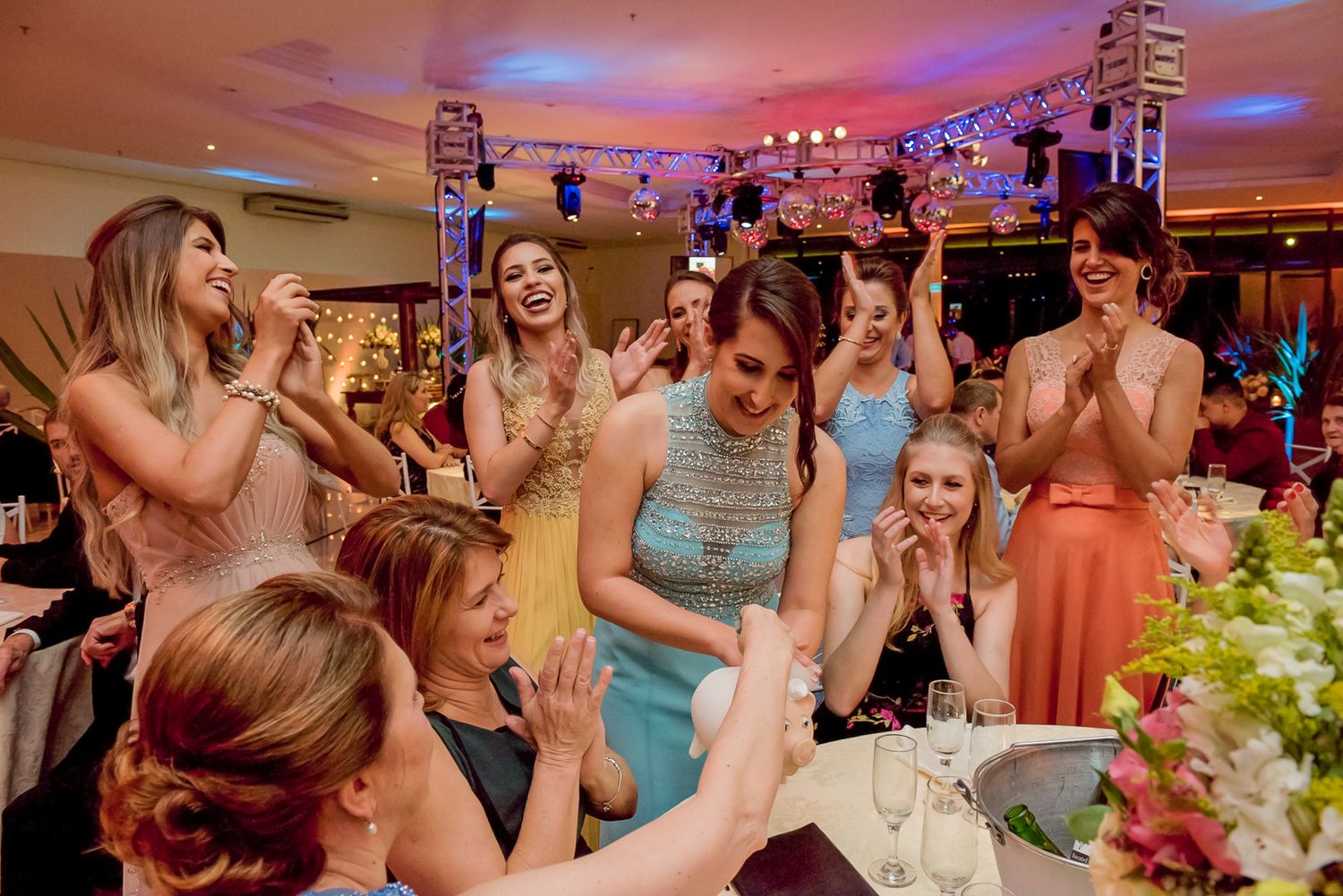 Wedding guests celebrating and cheering at a reception table with festive lighting.