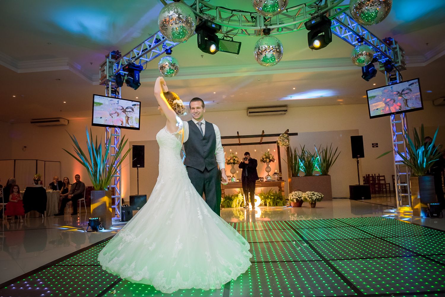 Couple performs their first dance on a lit-up checkered dance floor with decorative lighting.