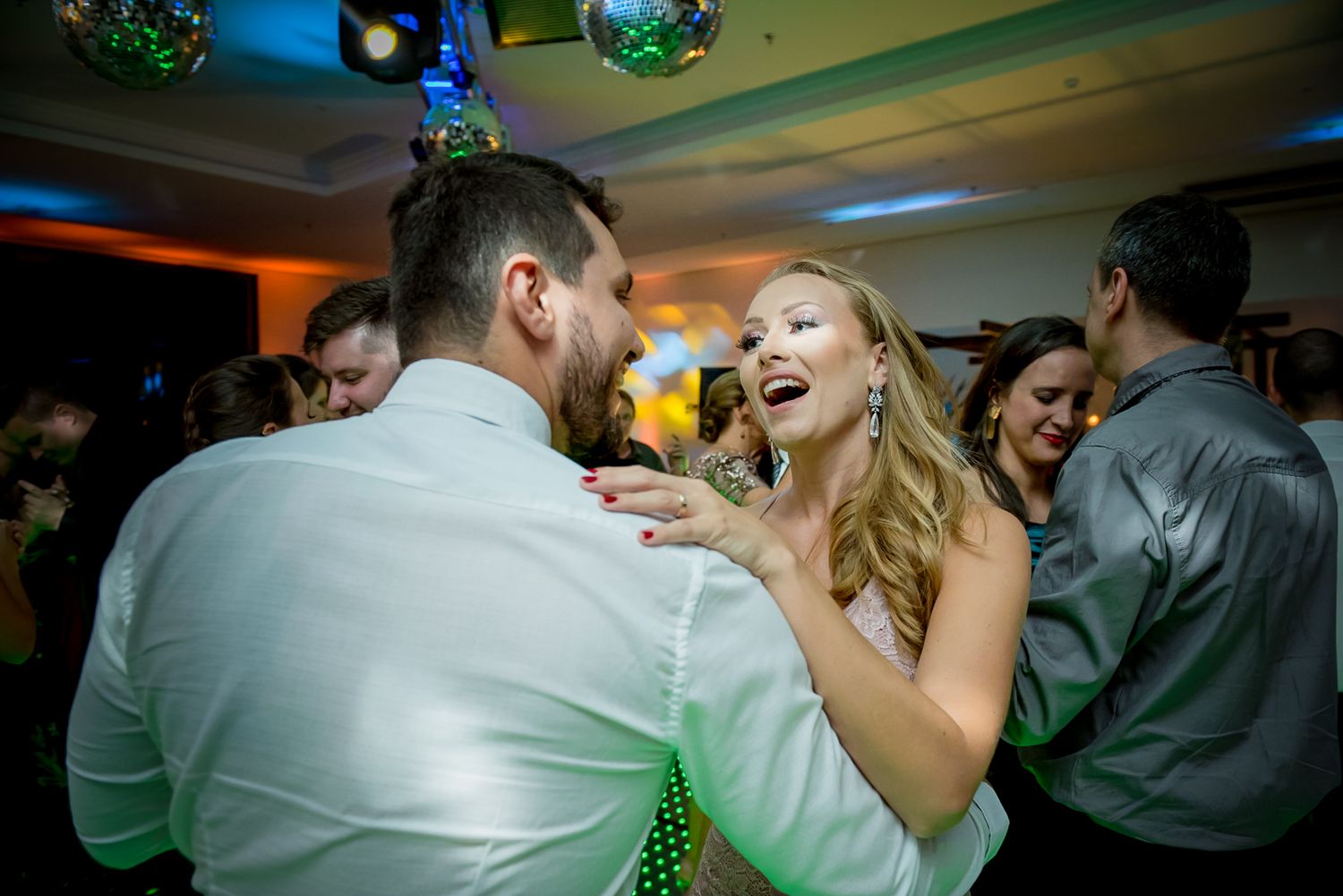Joyful dancing and celebration during the wedding reception under colorful venue lighting.