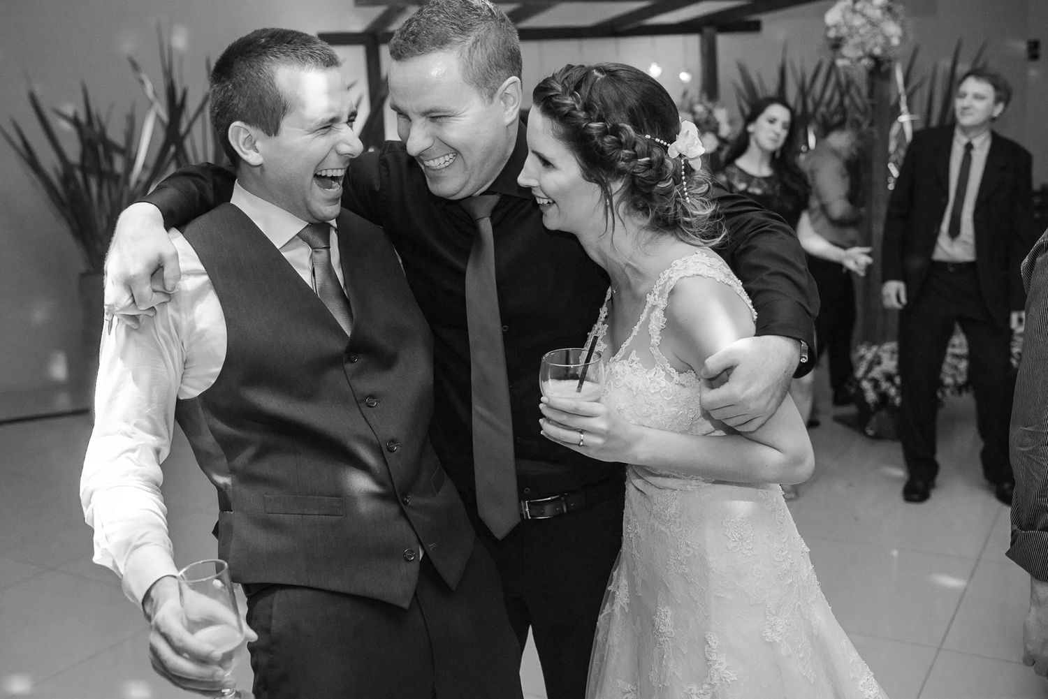 Three wedding guests share an intimate moment of laughter during the reception celebration.