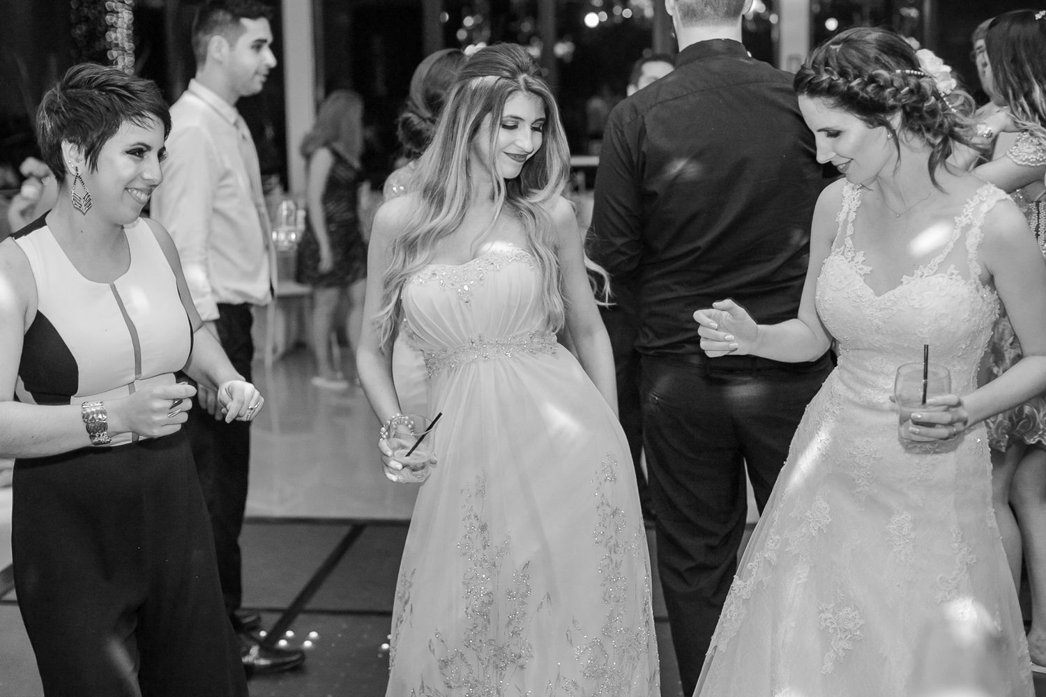 Wedding party members in elegant dresses dance and socialize at an indoor reception.