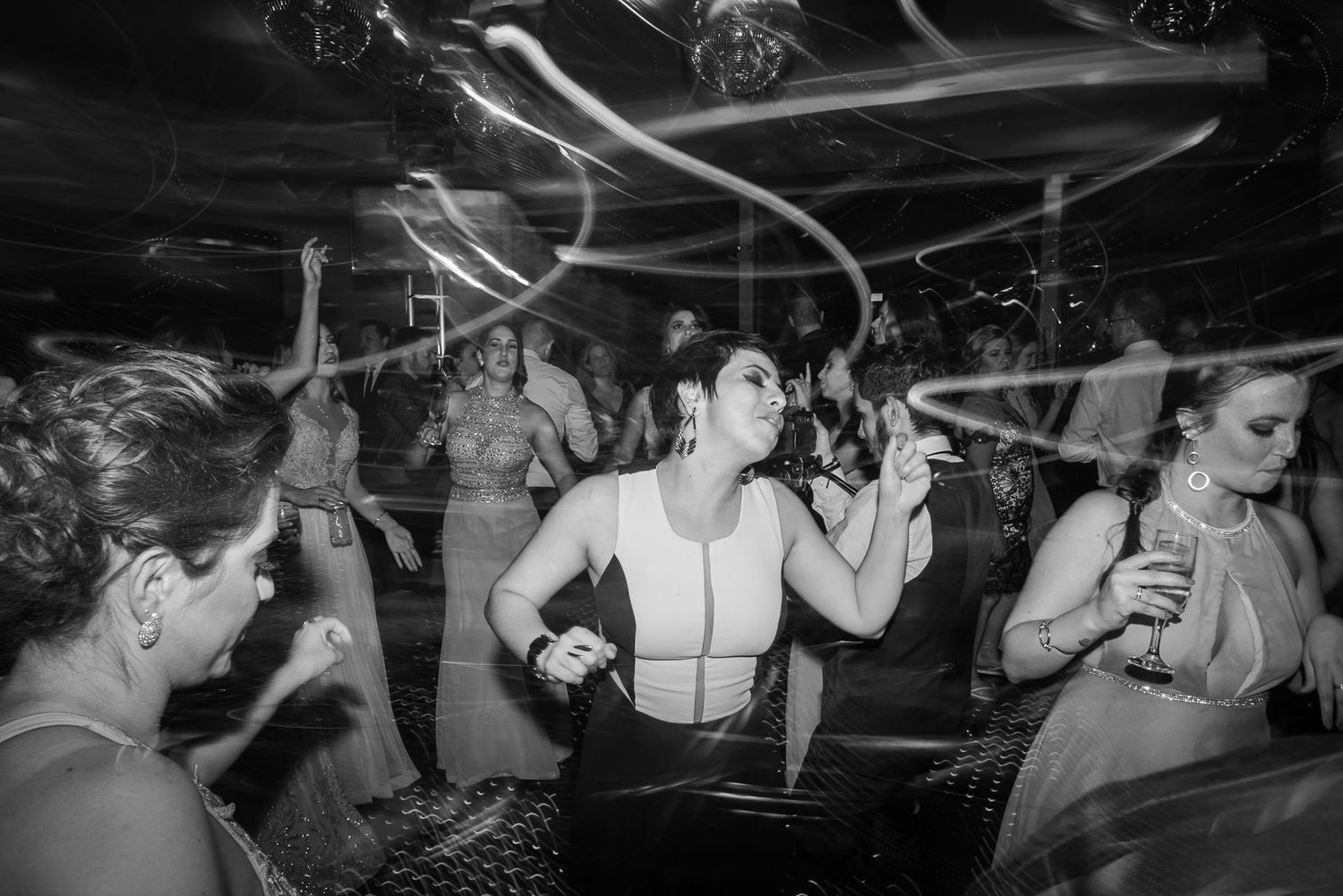 Wedding guests dancing enthusiastically under decorative lights at nighttime celebration.