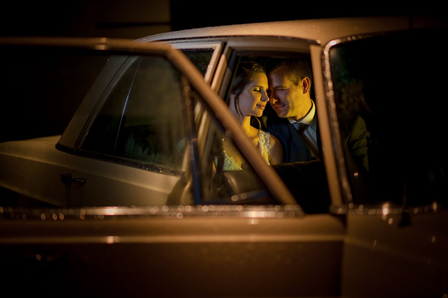 Romantic nighttime moment captured through car window at wedding celebration.