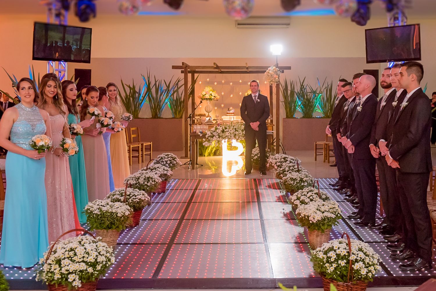 Wedding ceremony setup with floral aisle decorations and wooden arch in indoor venue.