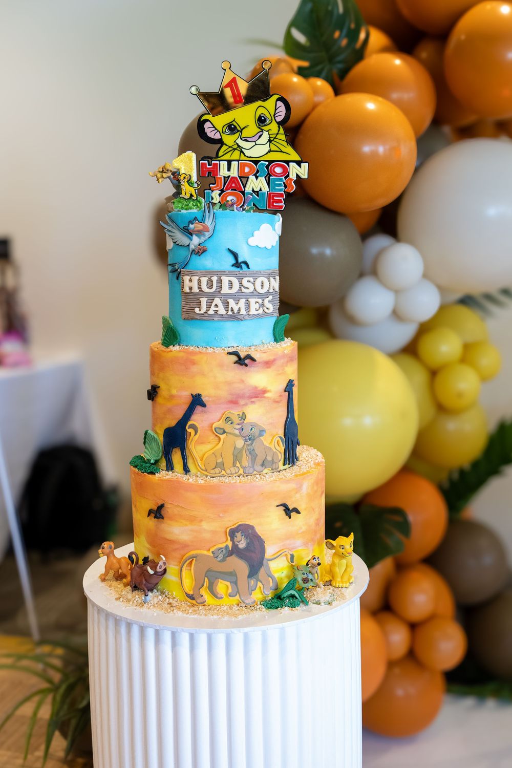 Three-tier Lion King themed birthday cake for Hudson James, decorated with safari characters and topped with Simba topper.