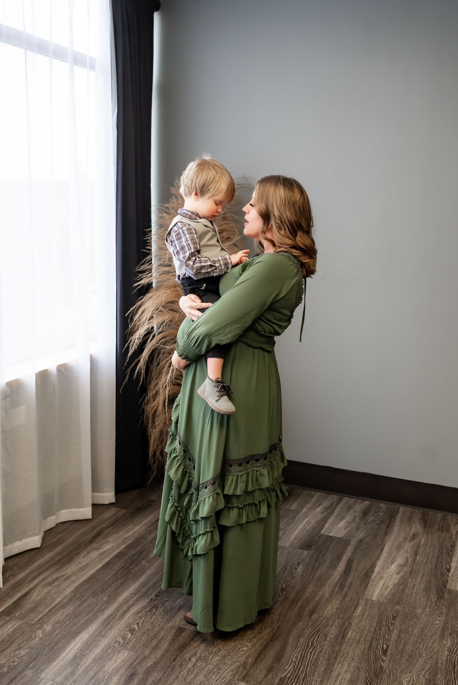 Sweet indoor family moment in sage green dress near window with pampas grass decor.