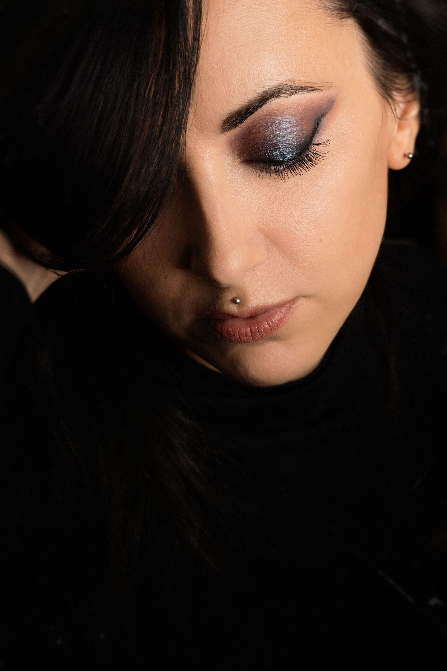 Close-up beauty shot featuring smokey eye makeup and a nose piercing in dark dramatic lighting.