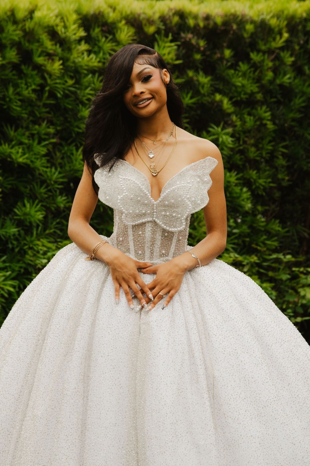 Woman in stunning pearl-embellished white ball gown wedding dress with butterfly bodice posing outdoors.